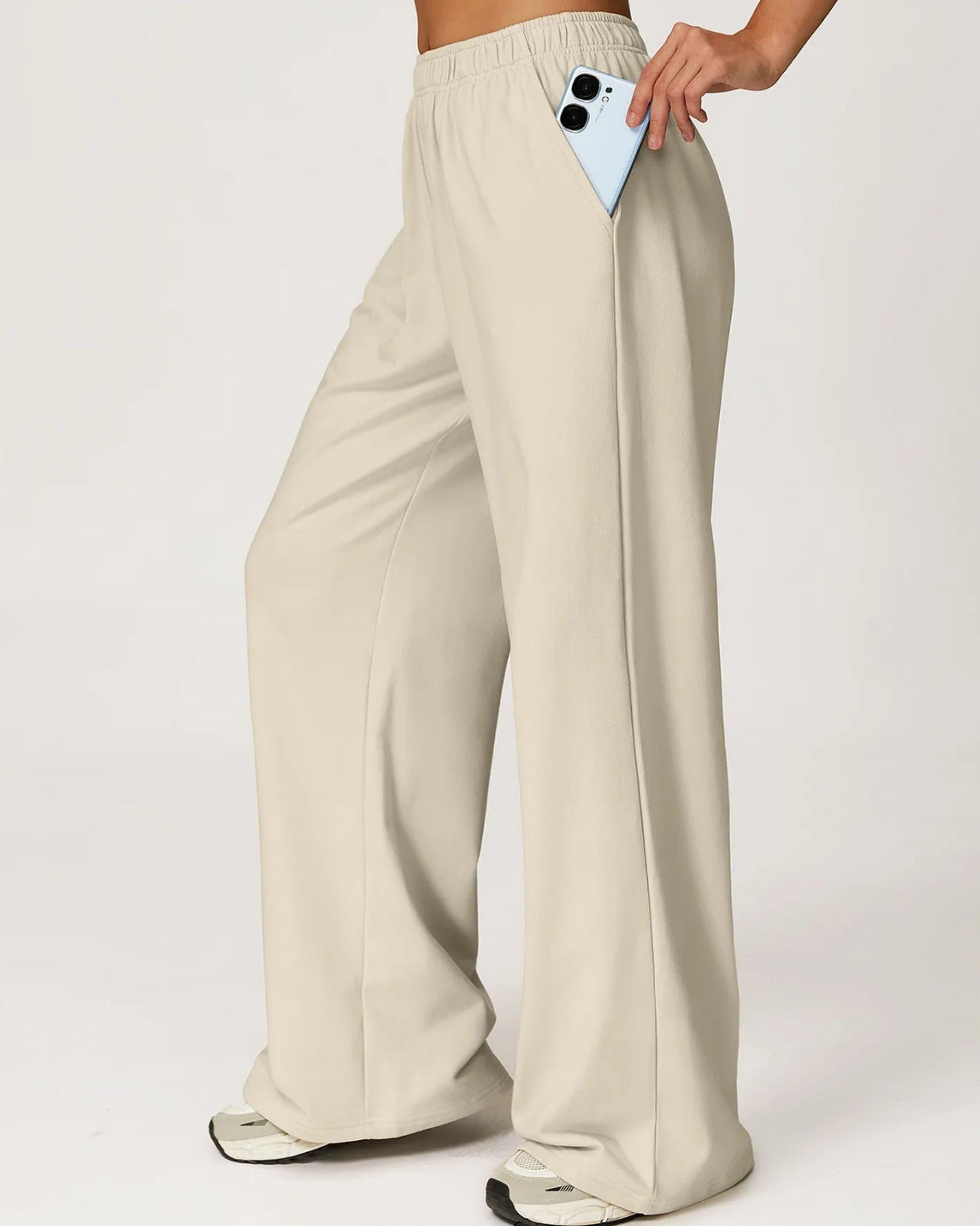 Seitenansicht der cremefarbenen High-Waist Wide Leg Hose, Hand steckt ein Smartphone in die tiefe Seitentasche, funktionale und stilvolle Sporthose - Ryze.